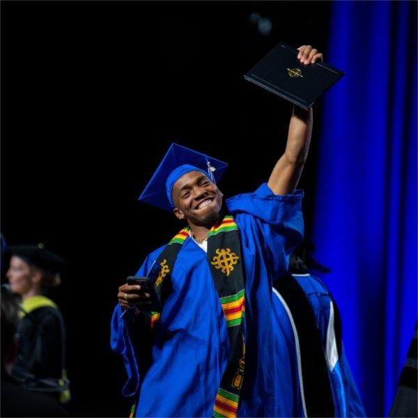 A graduate proudly holds up his diploma as he crosses the stage during Commencement.